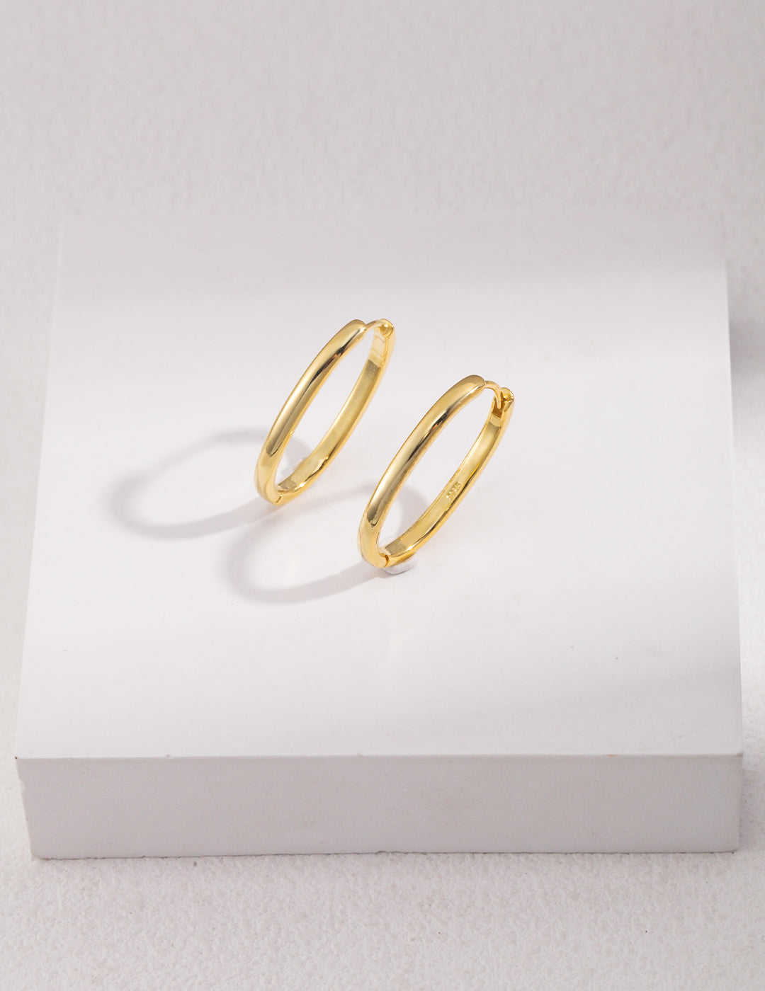 Two shiny gold hoop earrings on white background.