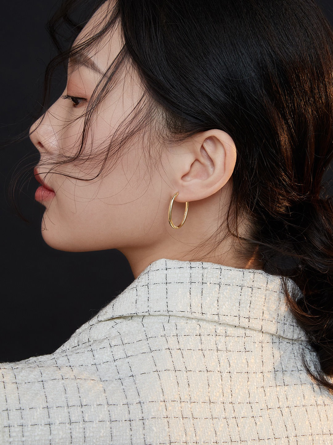 A model wearing a white blazer and gold hoop earrings, exuding elegance and style.