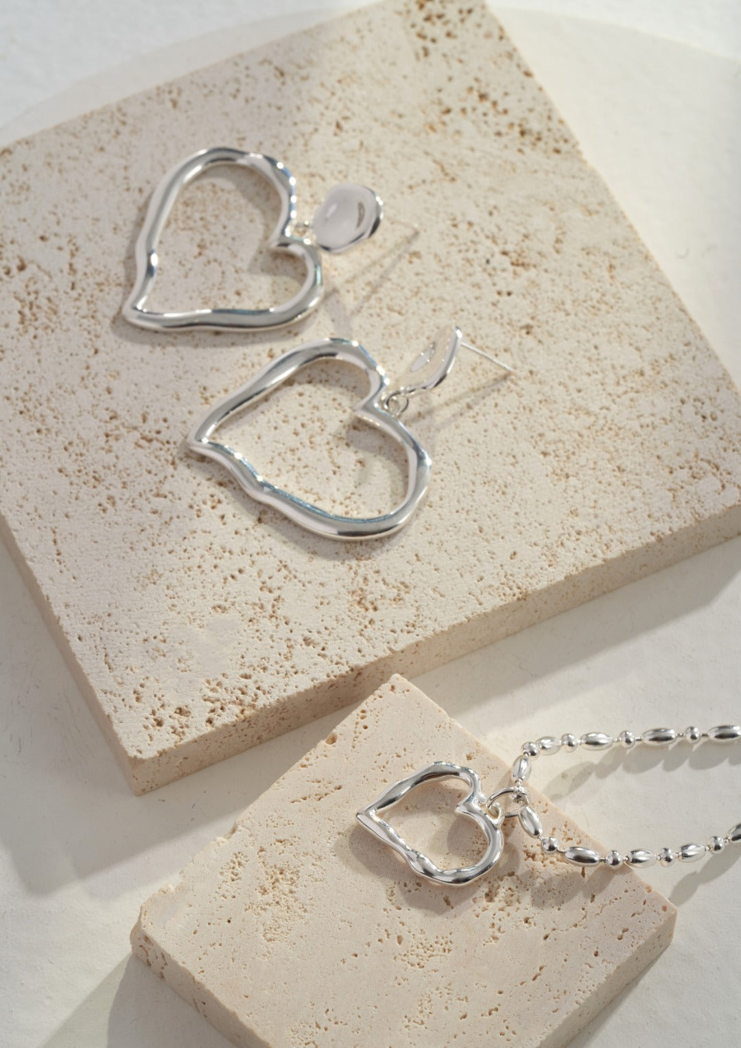 Stylish silver heart necklace and earrings set featuring heart shaped pendants on marble surface.