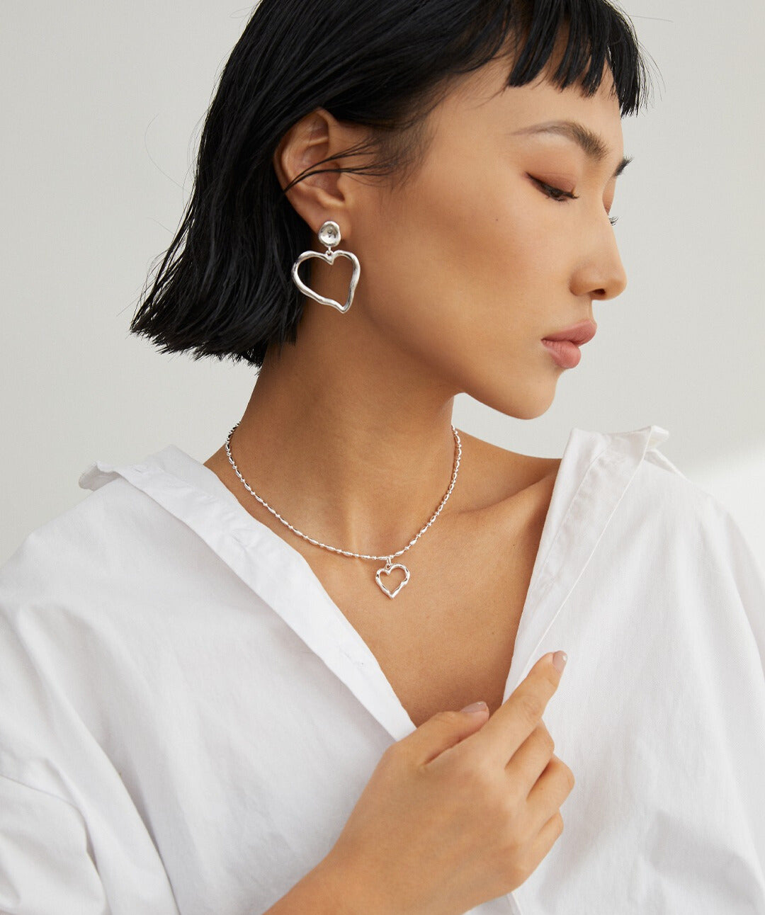 Stylish woman wearing white shirt and silver heart necklace with matching earring.