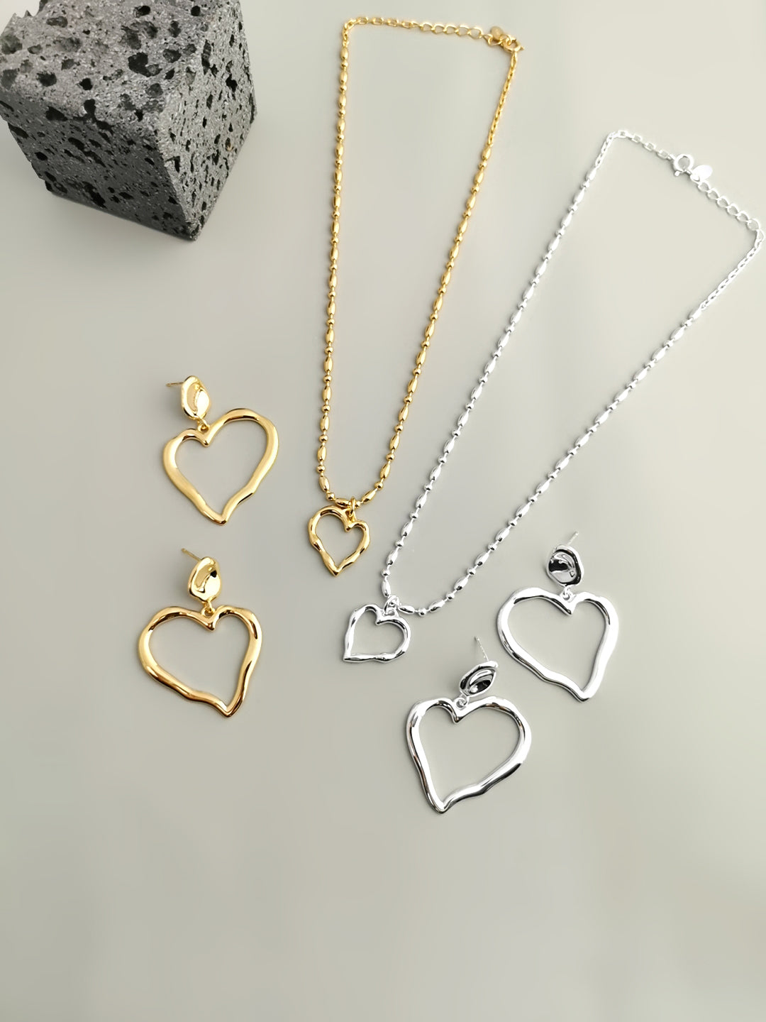 Collection of heart charms jewelry featuring silver and gold asymmetric necklace and earrings.