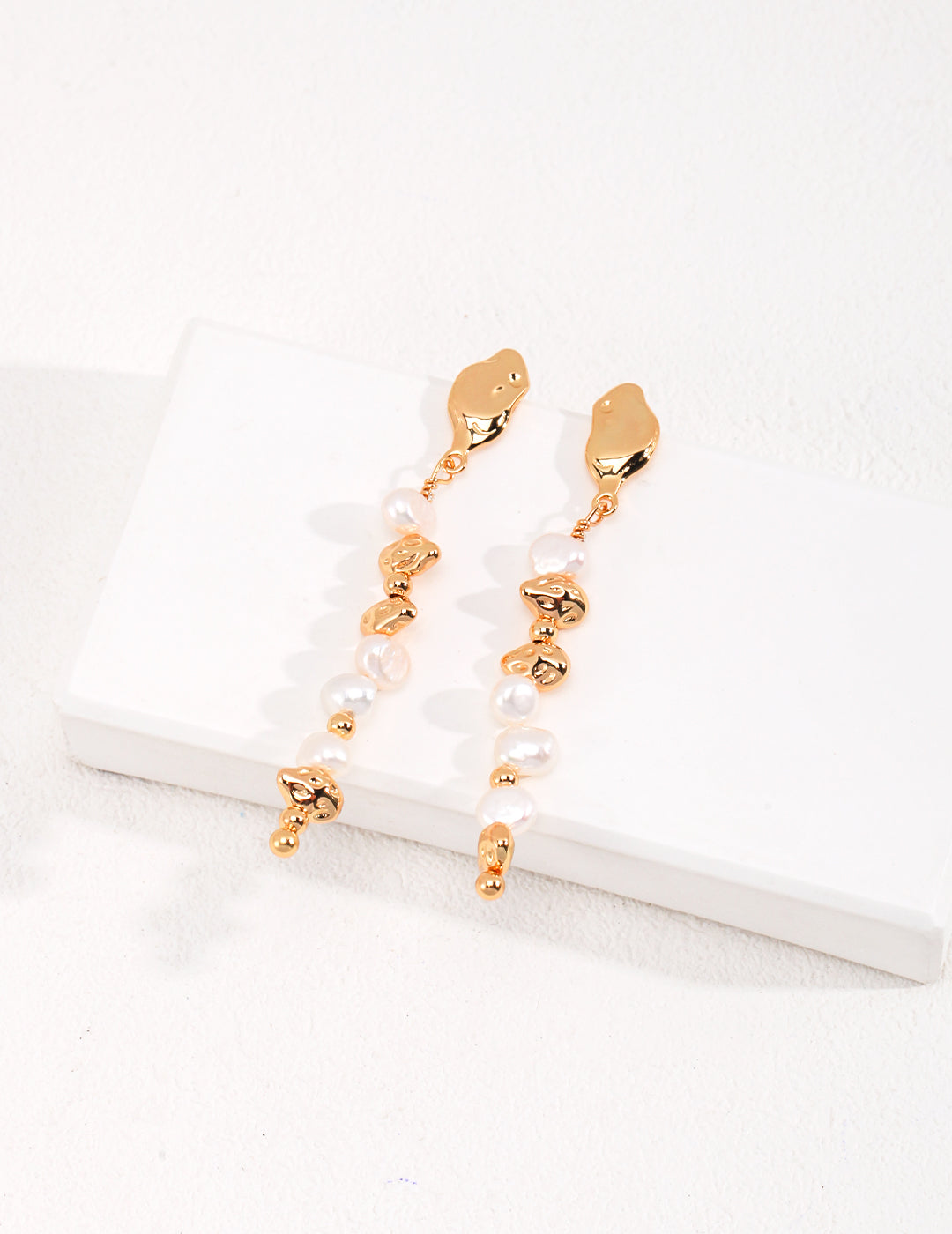 Elegant gold earrings with baroque pearl beads on white background.