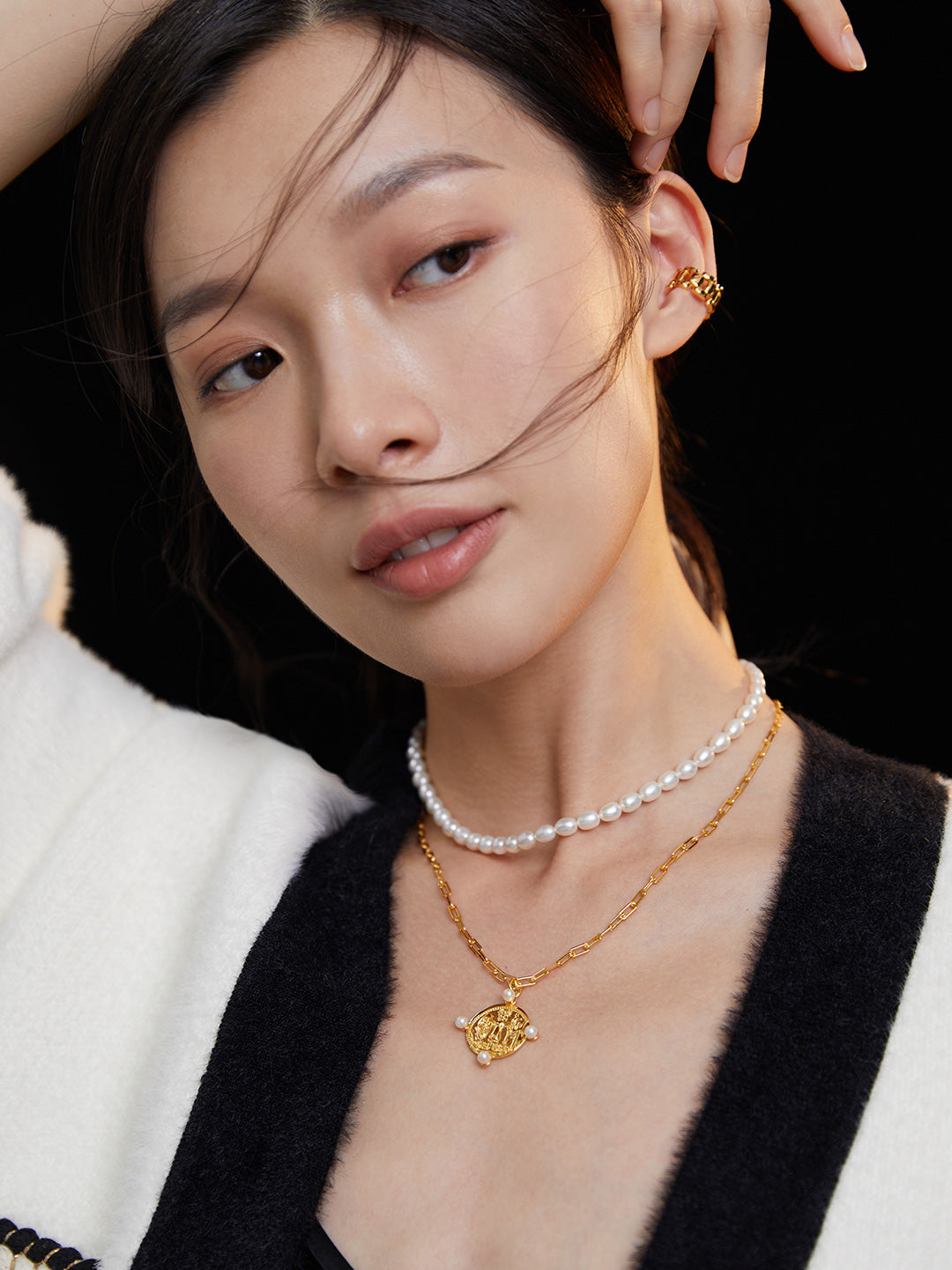 Woman in white sweater accessorized with layered necklaces, featuring a gold coin pendant and freshwater pearls.