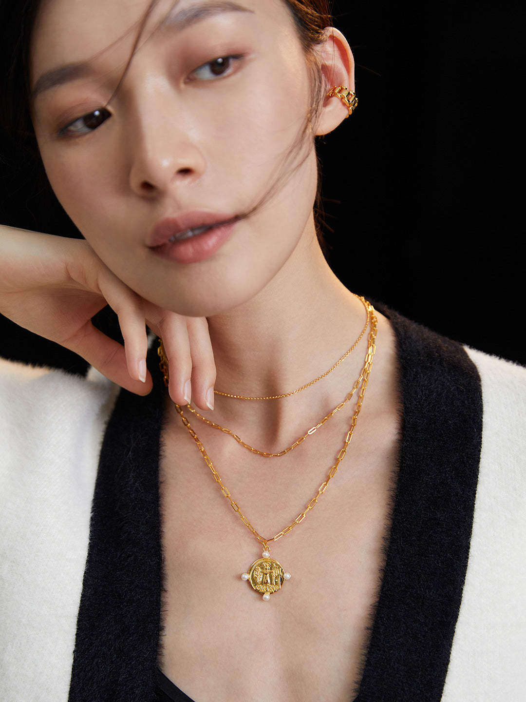 A fashionable lady wearing a white sweater and layered necklaces adorned with a gold coin pendant and freshwater pearls.