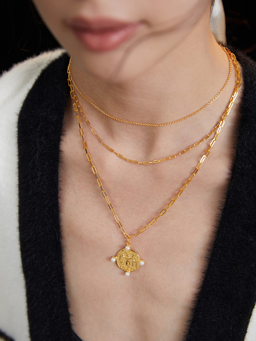 A model wearing layered gold chain necklaces with a gold coin pendant, and freshwater pearls.