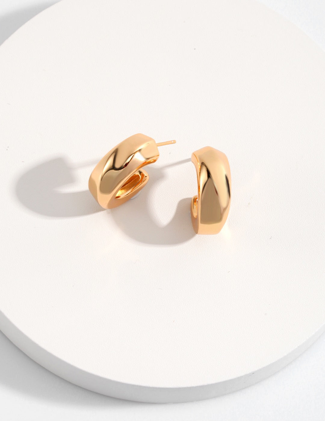 A pair of gold hoop earrings, with a thick design, beautifully displayed on a white surface, radiating sophistication.