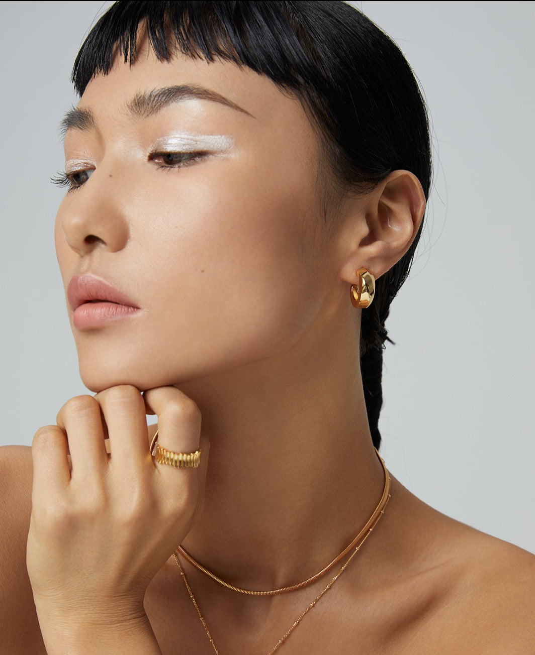 Stylish woman accessorized with gold necklace, featuring gold thick hoop earring.