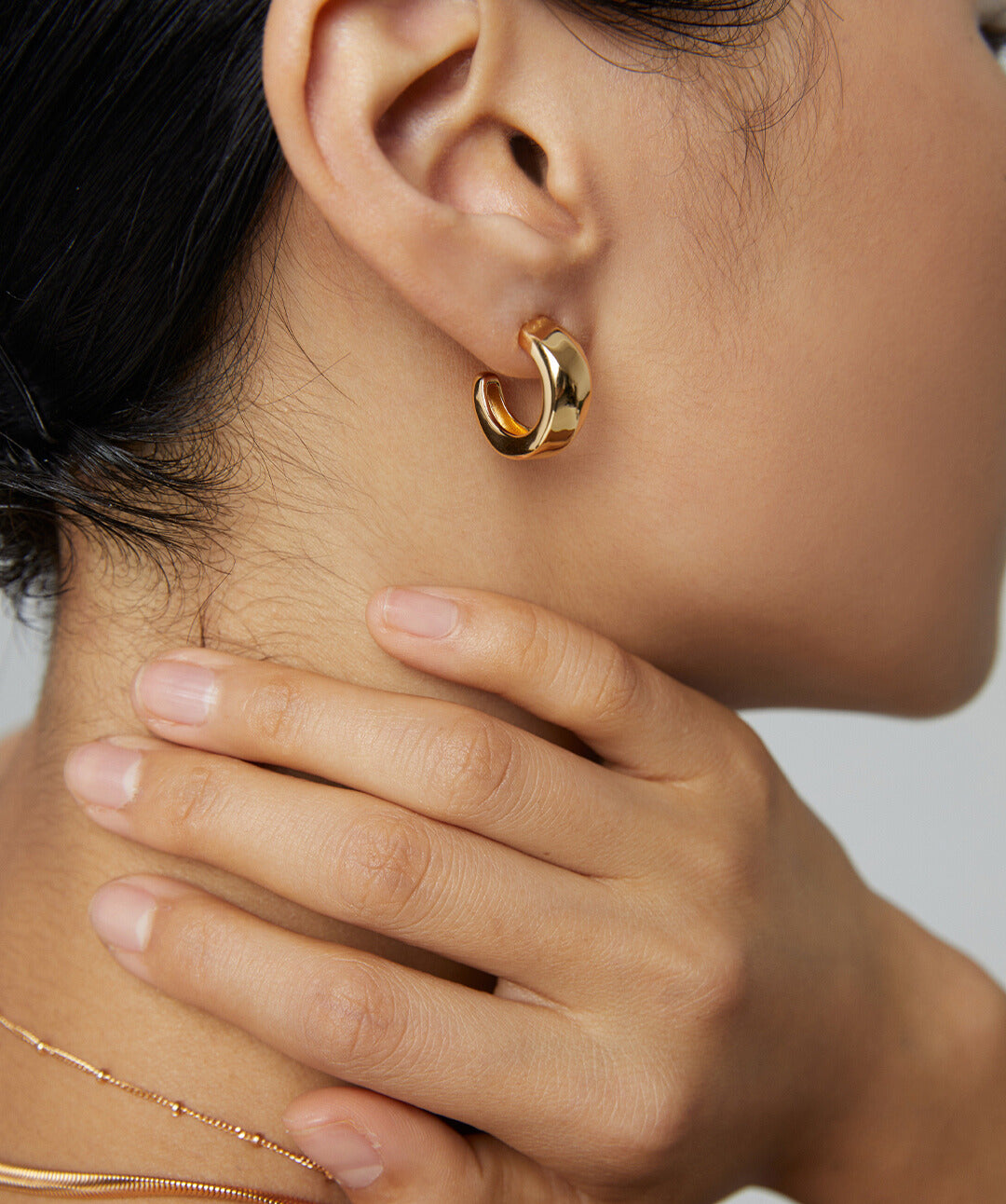 A woman wearing gold hoop earring and a matching necklace, showcasing a stylish and elegant look.