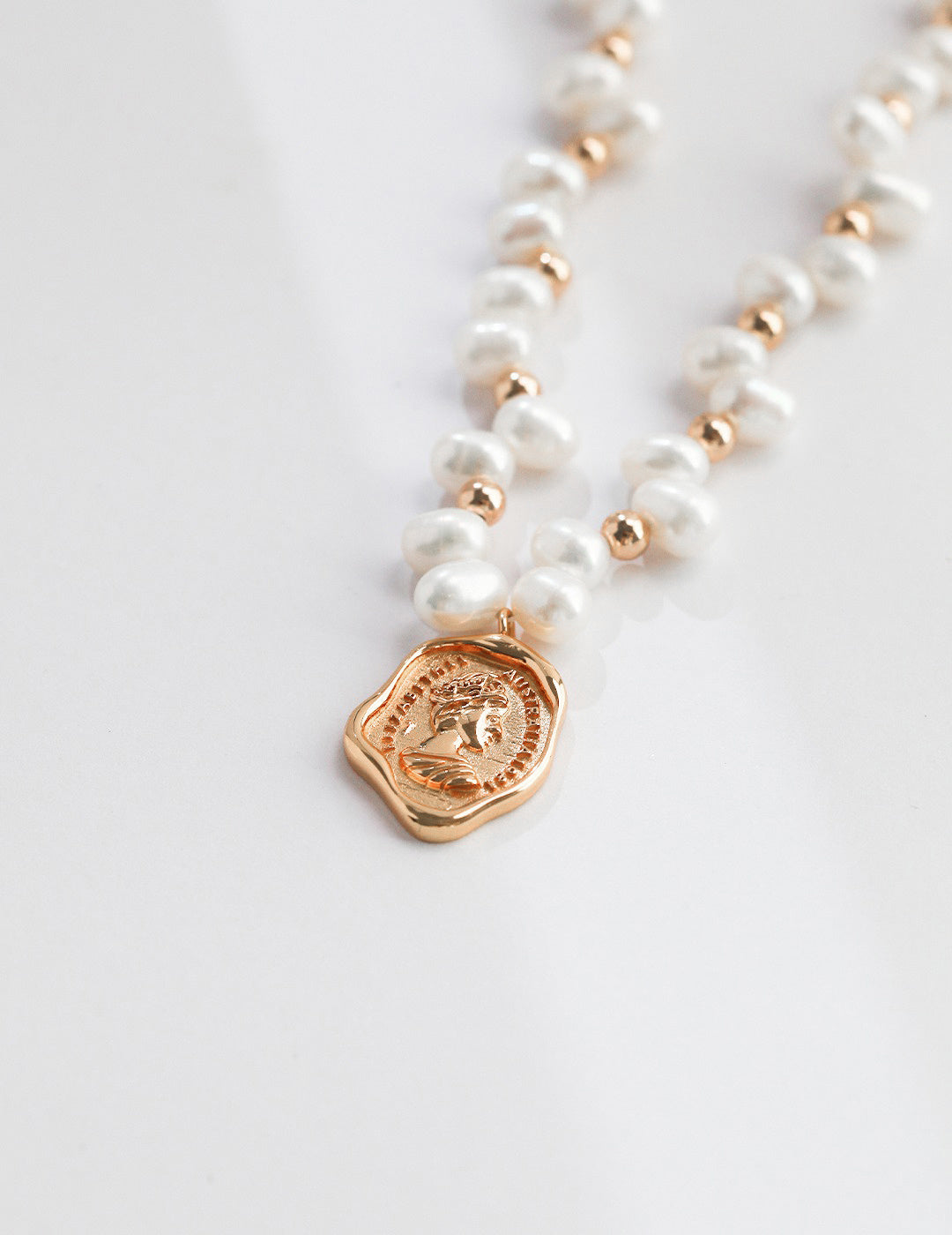 Detailed view of a pearl necklace adorned with a gold coin charm, highlighting its luxurious and classic design.