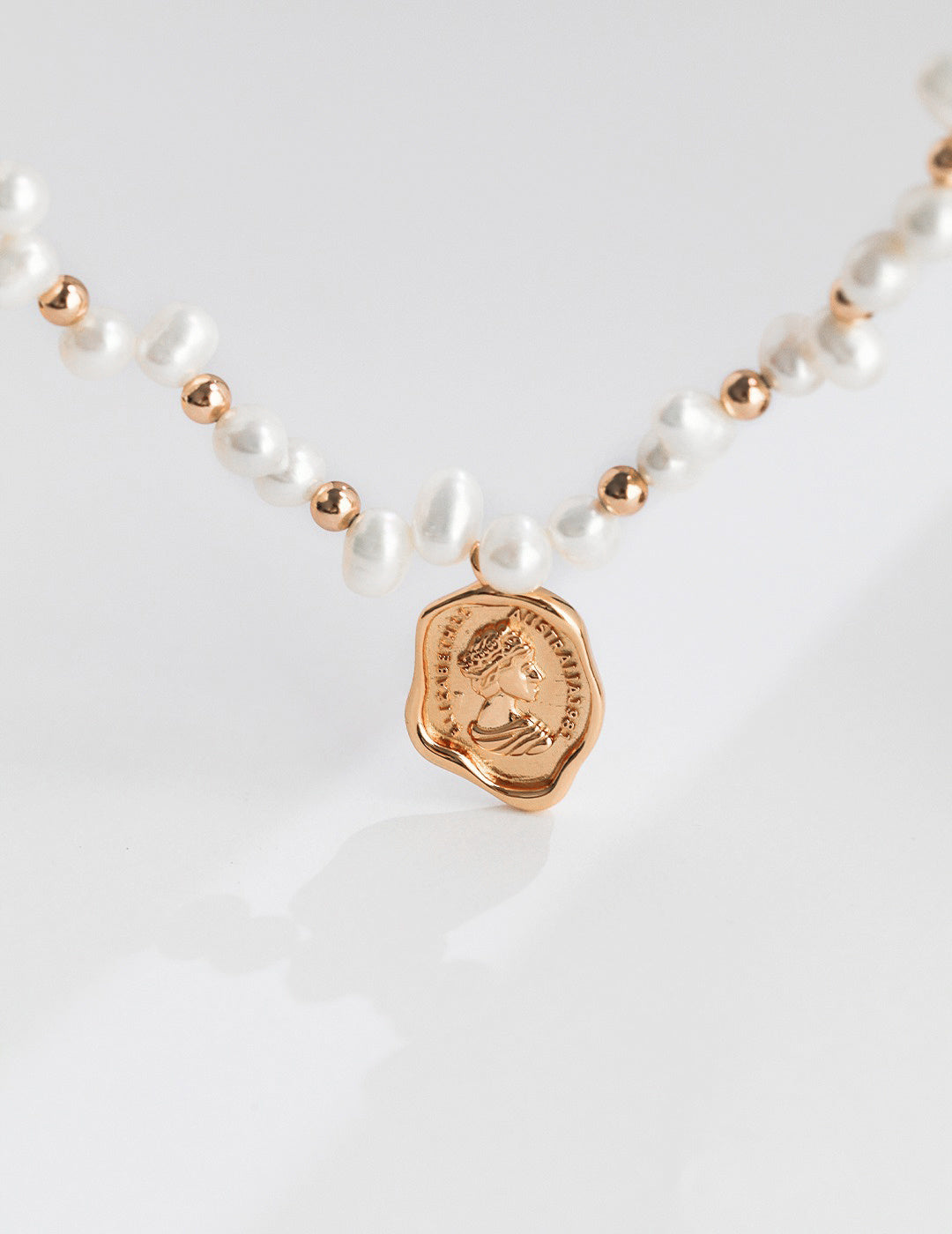 Close-up of a gold coin charm elegantly hanging from a delicate pearl necklace, showcasing its luxurious detail.