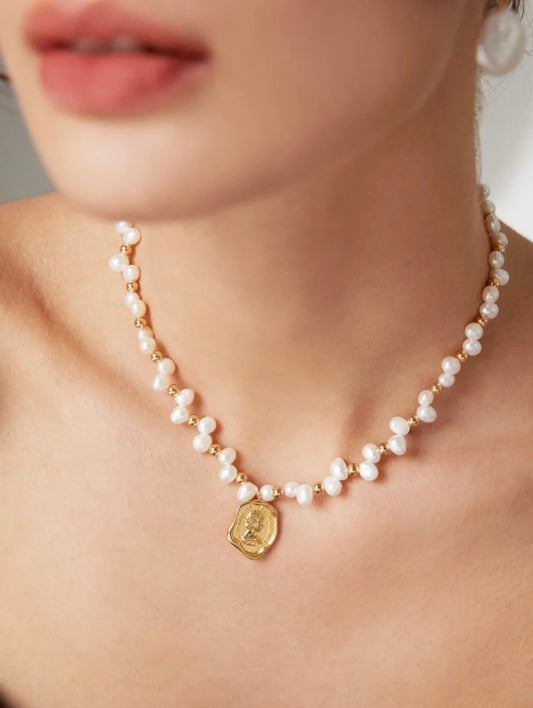 A woman showcasing a beautiful pearl necklace complemented by a gold coin charm.