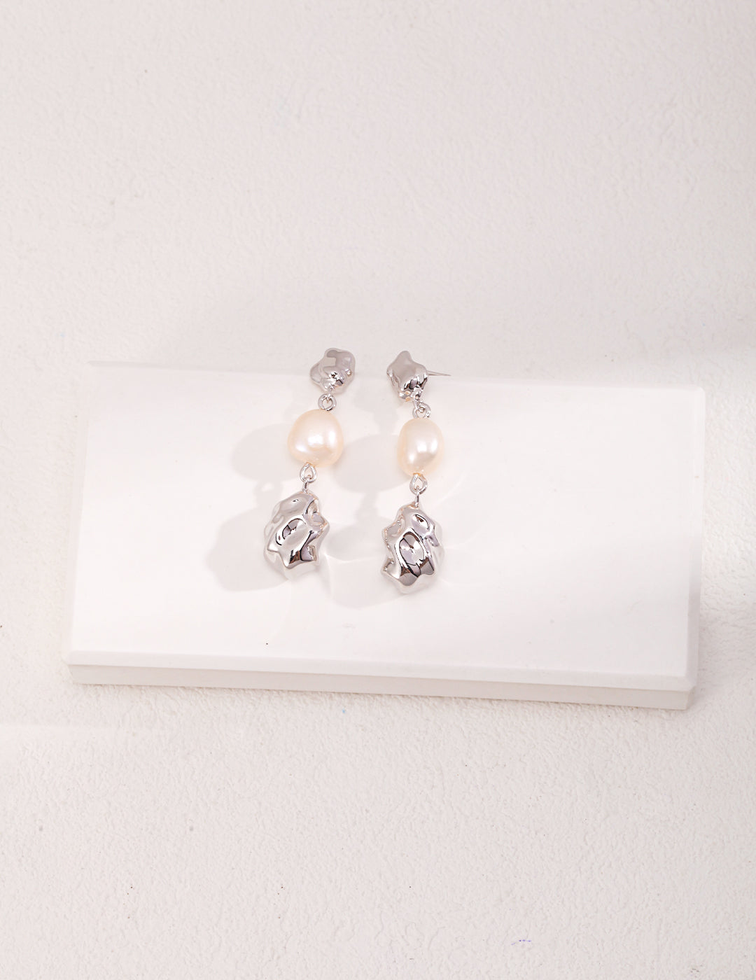 A stunning pair of pearl and silver earrings resting on a pristine white surface.