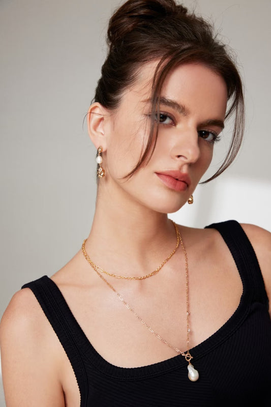 An elegant model in a black top adorned with a gold necklace and earrings, highlighting a chic and fashionable look.
