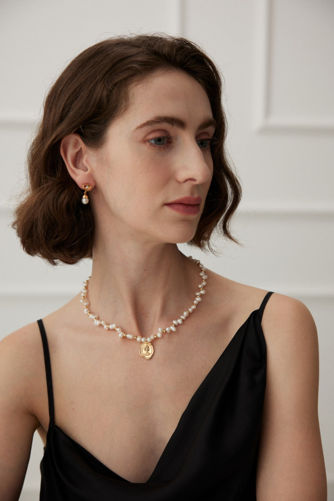 Lifestyle shot of a woman wearing the Catarina pearl coin necklace and matching pearl drop earrings for a sophisticated, executive look.