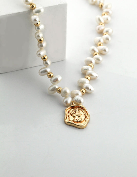 The Catarina necklace with lustrous pearls and gold bead accents draped over a minimalist white pedestal.