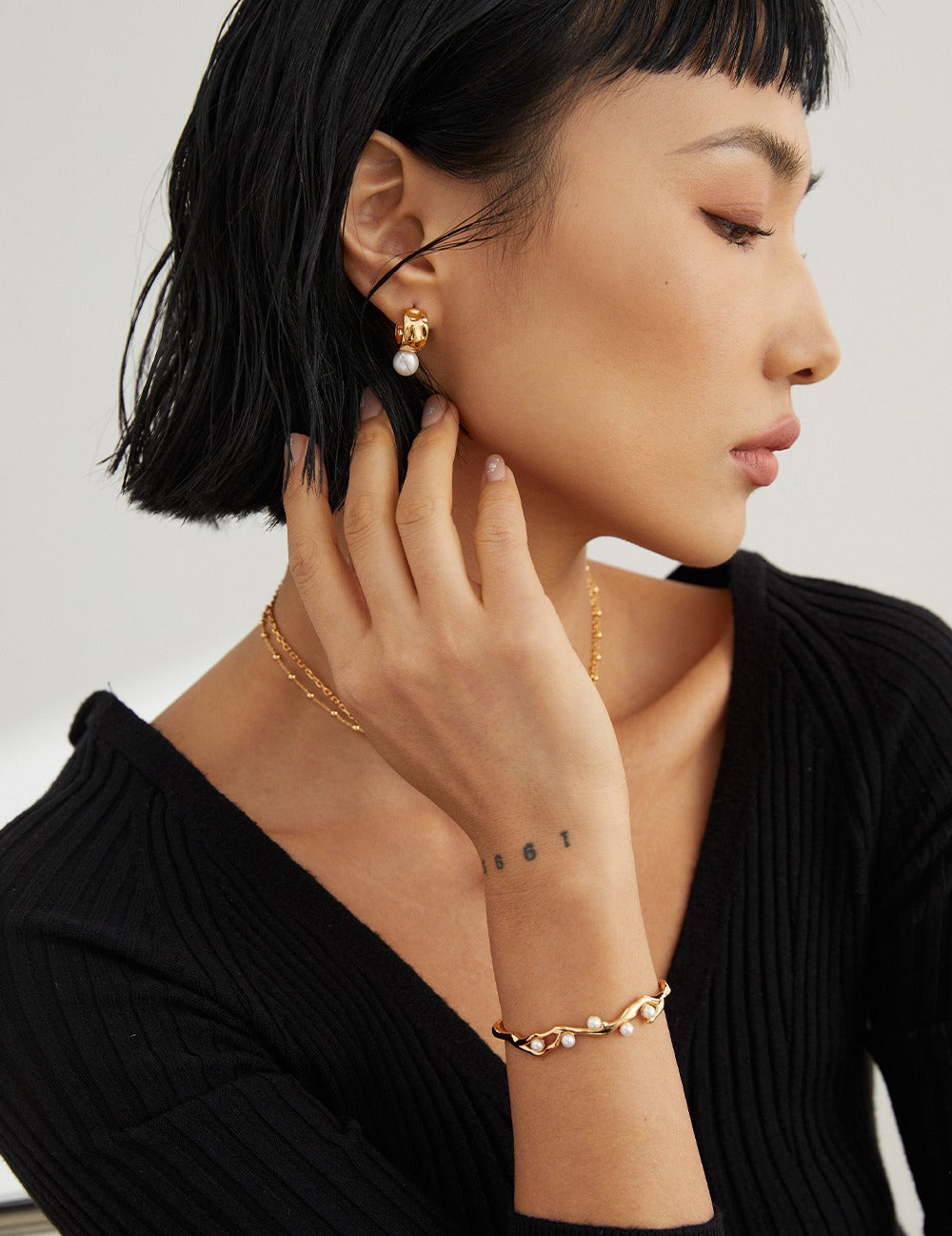 Model in black sweater wearing 18k Gold Vermeil pearl hoop earrings and pearl bracelet from Mezuille.