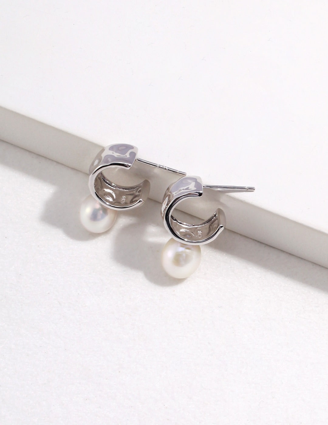 Pair of silver C-shaped hoop earrings with pearls from Mezuille on white surface.