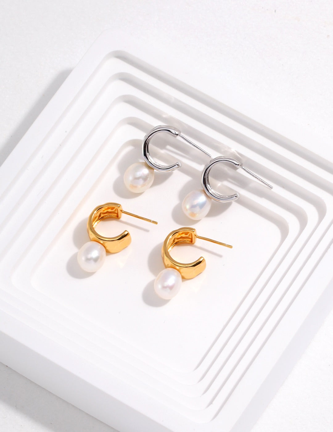 Two pair of gold and silver hoop earrings with pearls from Mezuille , placed on white surface