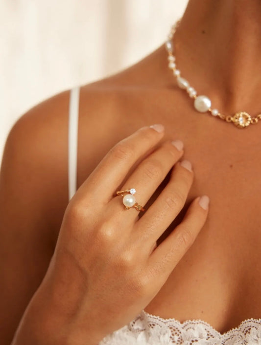 A woman in a white lace dress and pearl necklace, featuring a minimalist ring, exudes elegance and style.