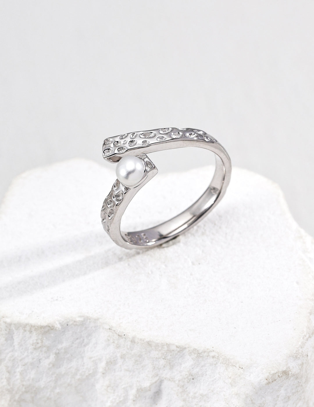 Silver open ring with a exquisite pearl on a white stone surface.
