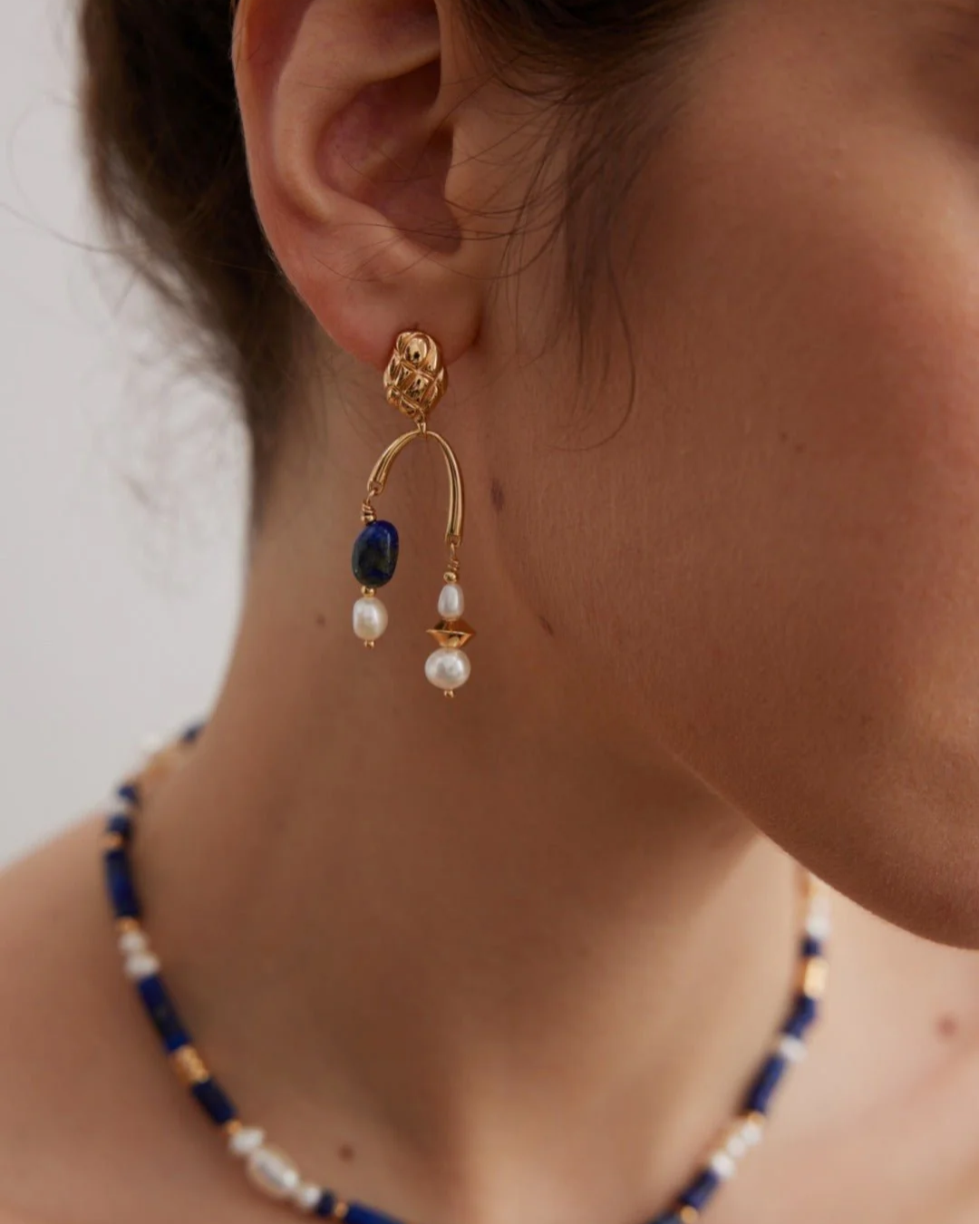 Close up shot of woman wearing an elegant blue and white earring crafted from lapis lazuli and pearls, perfect for adding a touch of sophistication.