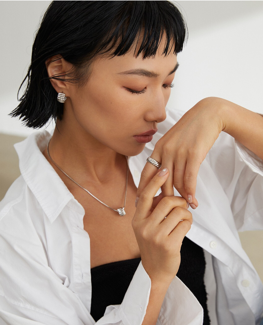 A woman in a white shirt wearing a silver ring, with matching earring and necklace.