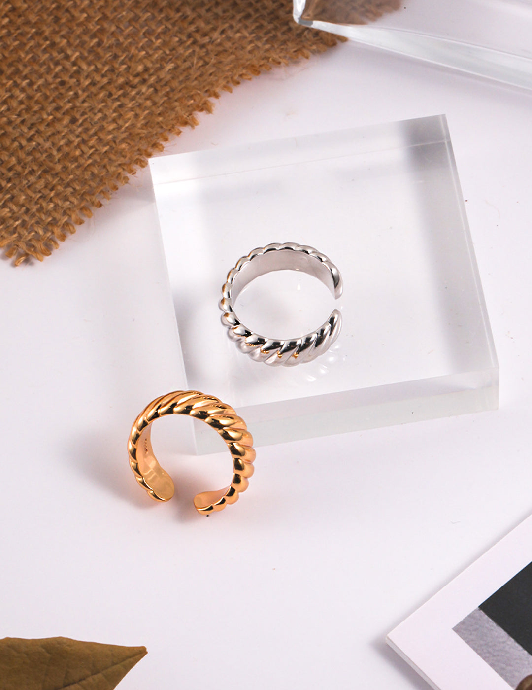 Two twisted rings, one gold and one silver, placed on a glass table.