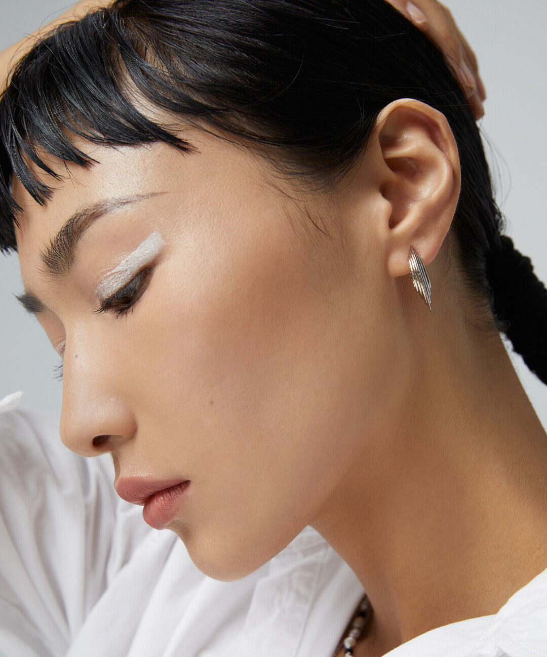 Woman in white top accessorized with silver disc earrings.