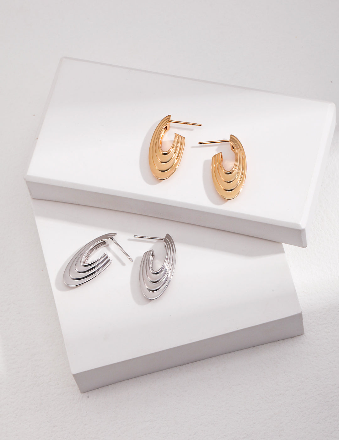 Two pairs of disc-shaped earrings in gold and silver on a white box.