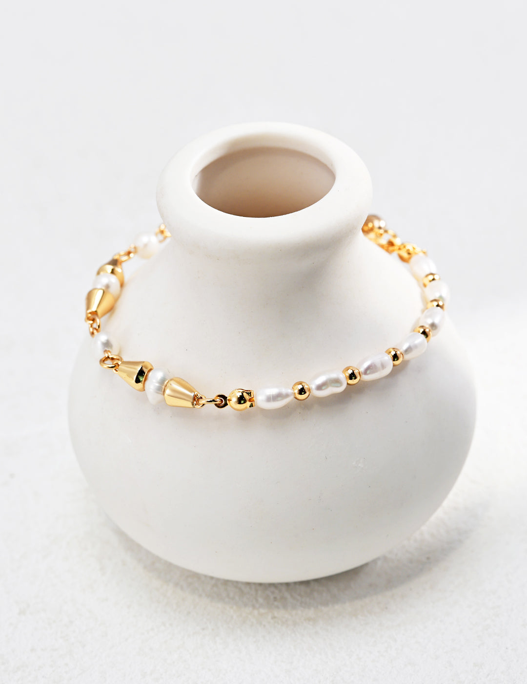 White vase with gold plated freshwater pearl bracelet on top.