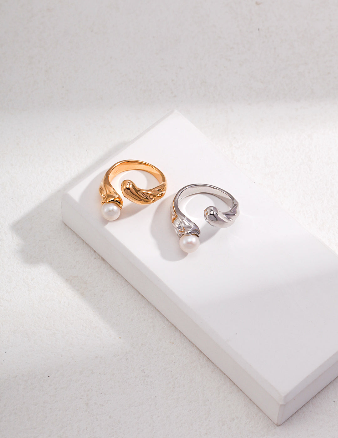 Stylish silver and gold rings featuring shimmering freshwater pearls on a white tabletop.