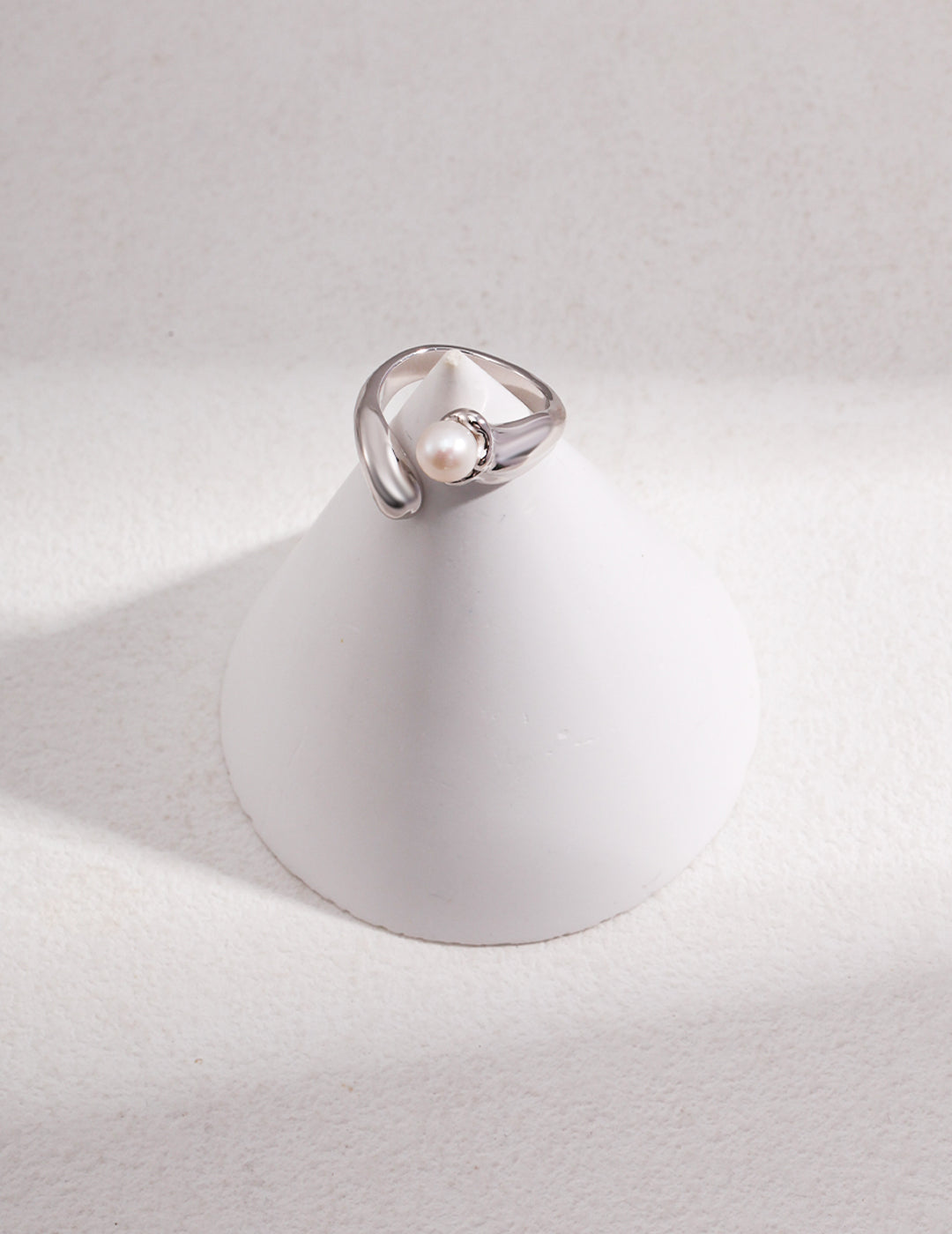 A silver ring with a freshwater pearl placed on a white cone.