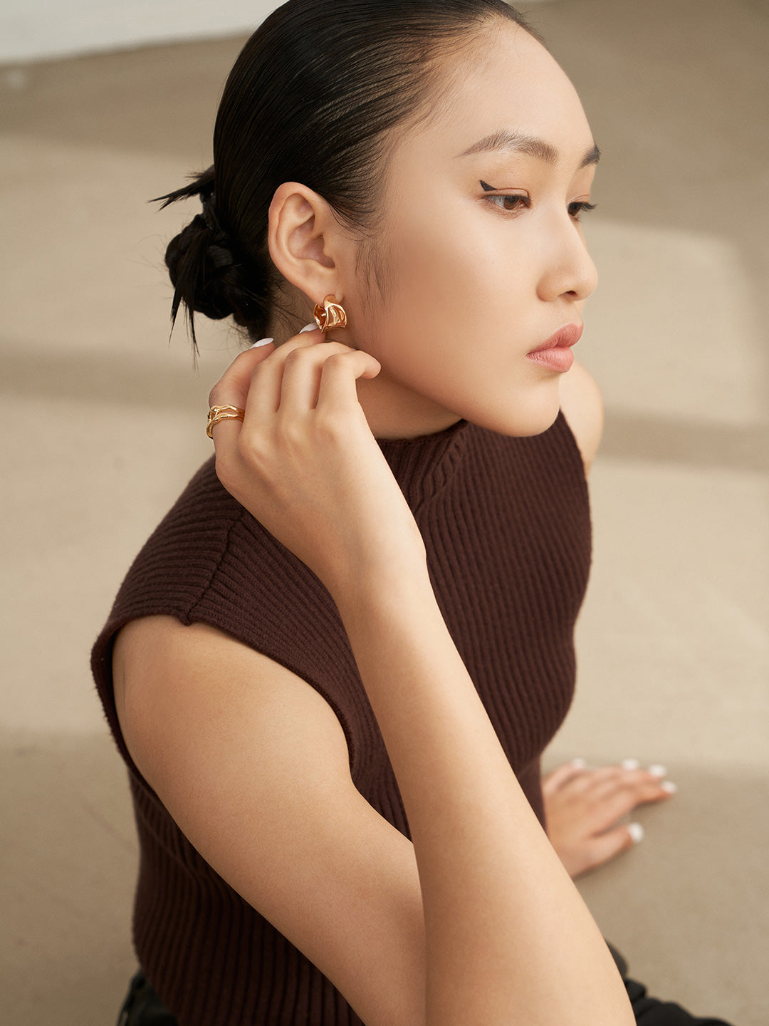 A woman in a burgundy top and black pants, showcasing gold earrings.
