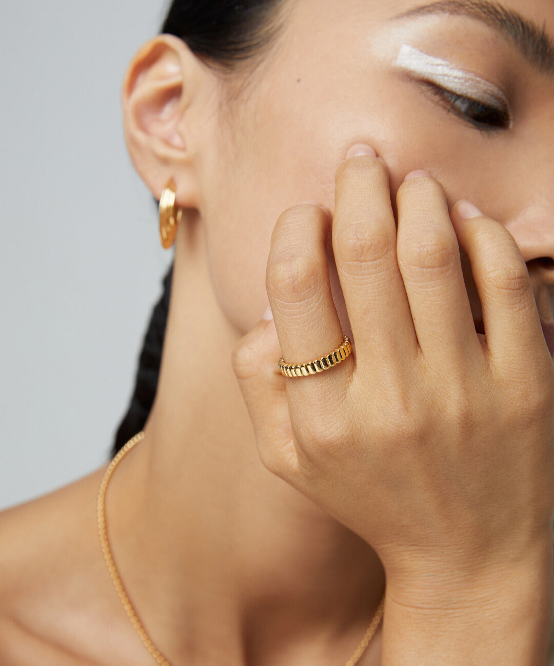 A woman wearing a stunning gold ribbed ring and other gold jewelry.