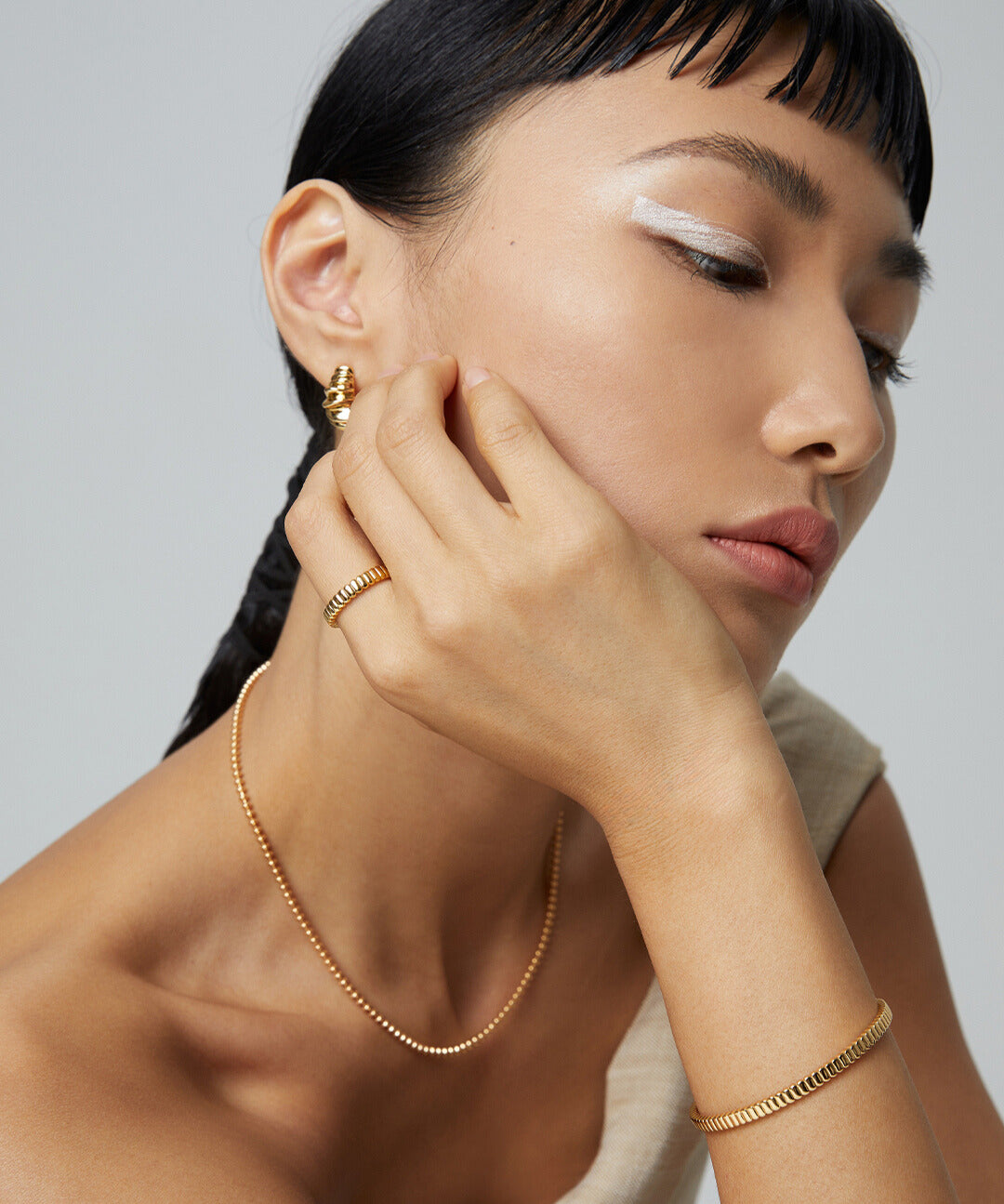 A woman wearing gold jewelry, including a bracelet and earrings, with a gold ribbed ring on her finger.