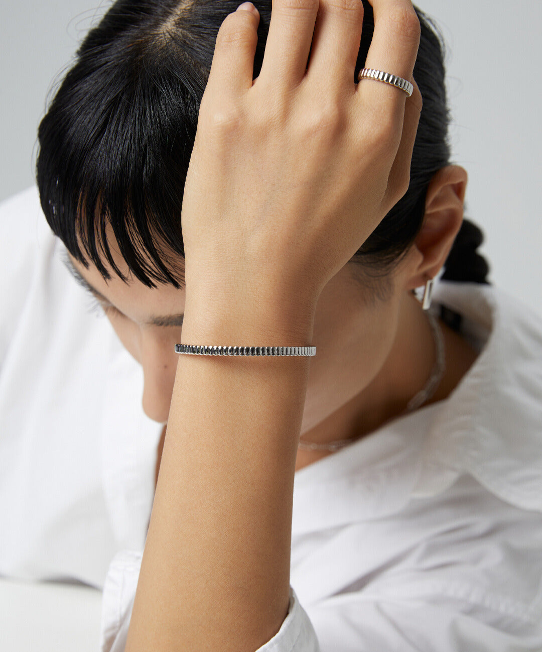 Woman in white shirt with silver bracelet and ribbed ring.