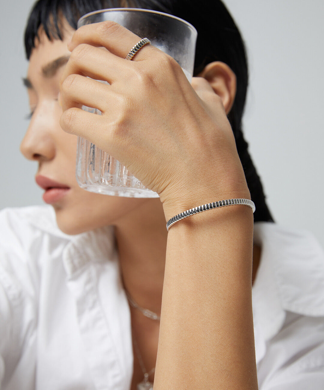 A woman wearing a glass bracelet and silver jewelry, including a silver ribbed ring.