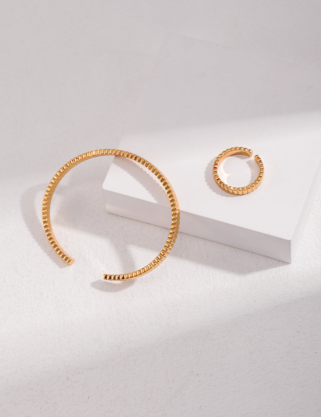 A gold ribbed ring and matching bangle elegantly displayed on a white surface.