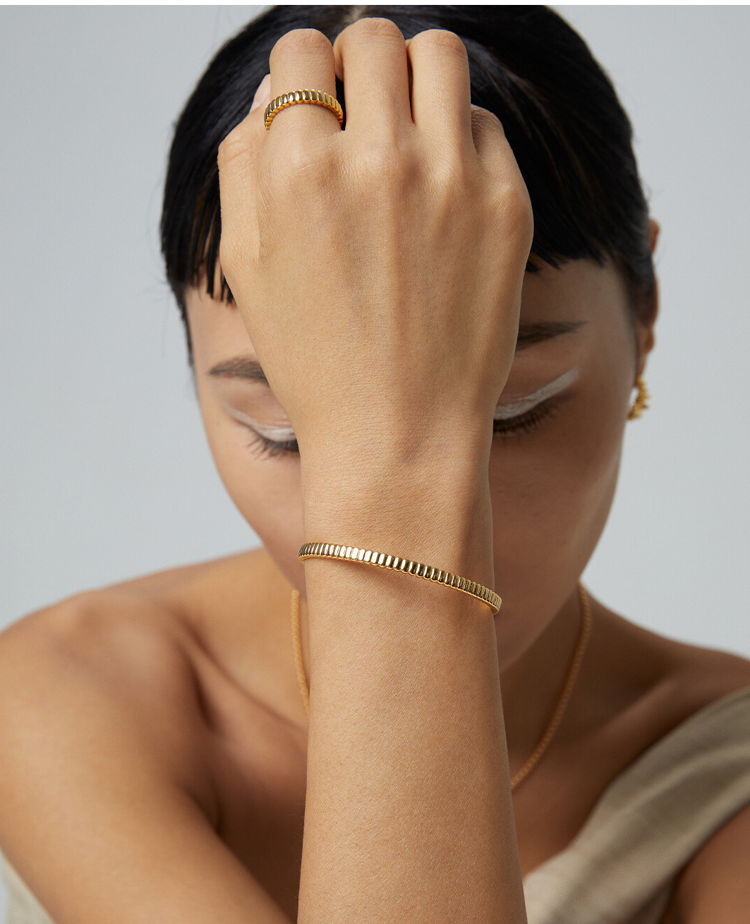 A woman wearing a gold bangle and a gold ring.