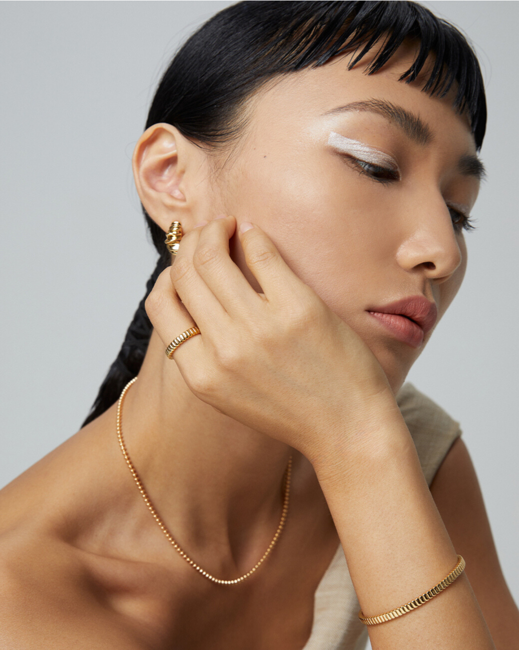 A woman adorned with a gold chain necklace, earrings, and a bangle.