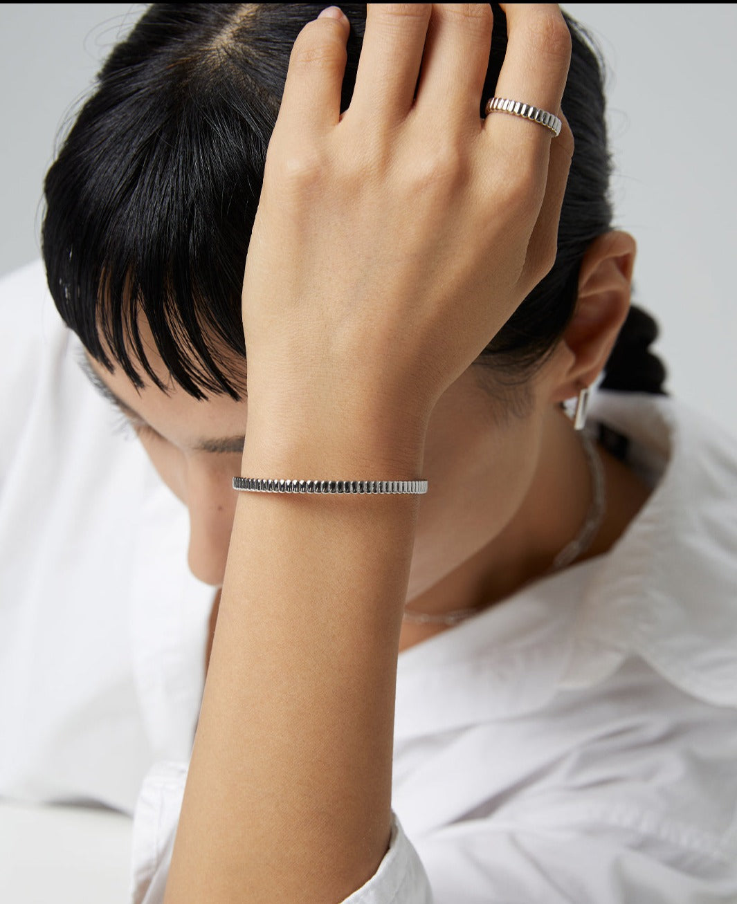 A woman wearing a silver bracelet and a white shirt, exuding elegance and style.