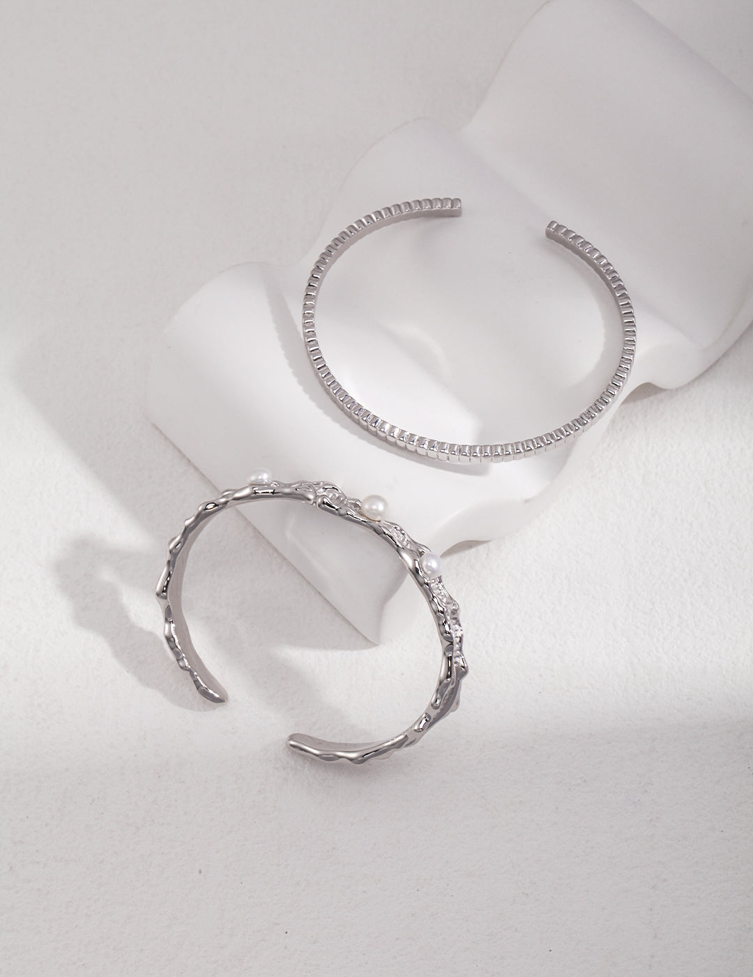 Two silver bracelets on a white surface: elegant accessories shining brightly, adding a touch of sophistication.