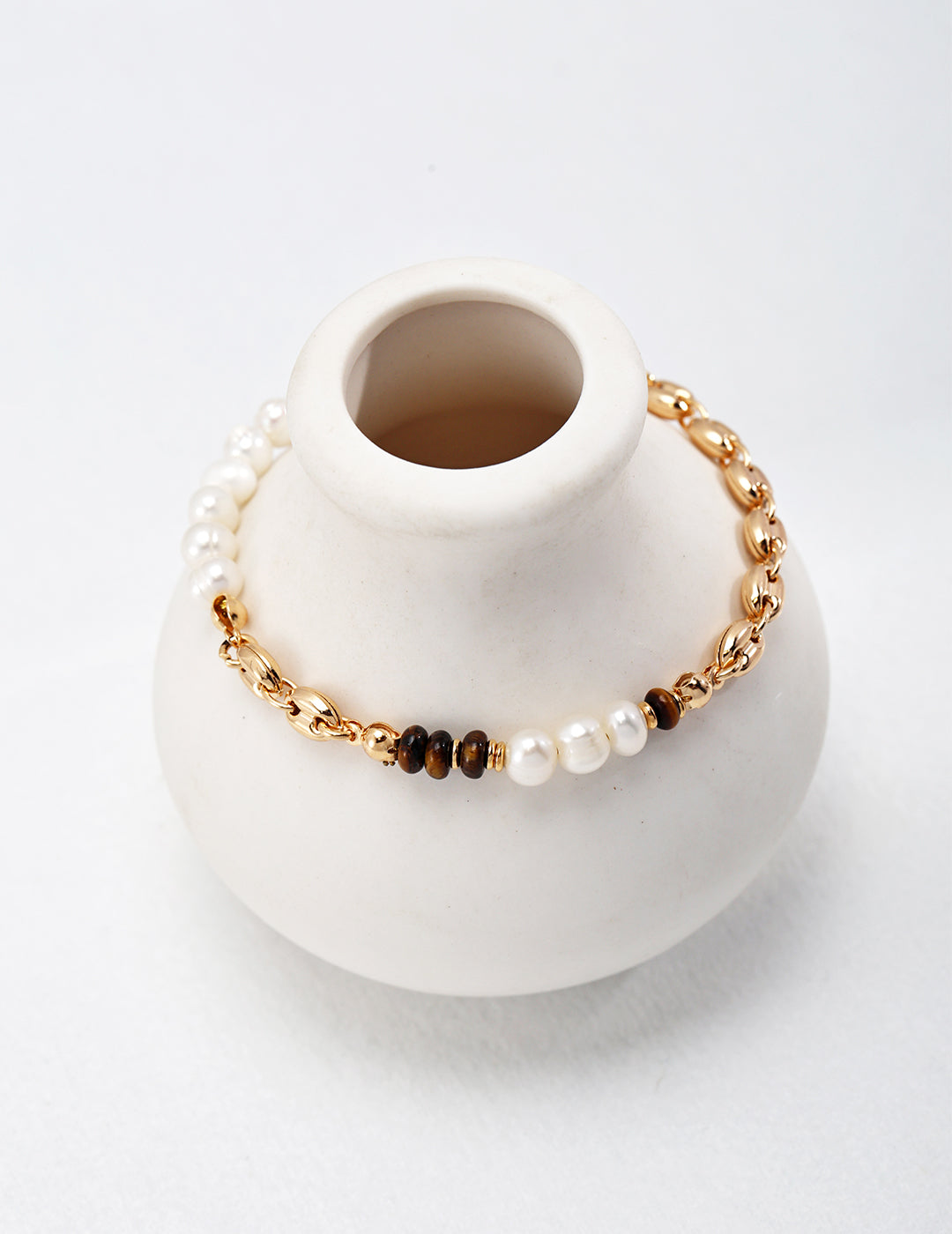 A white vase with a gold chain and pearl bracelet, adding elegance and charm to any space.