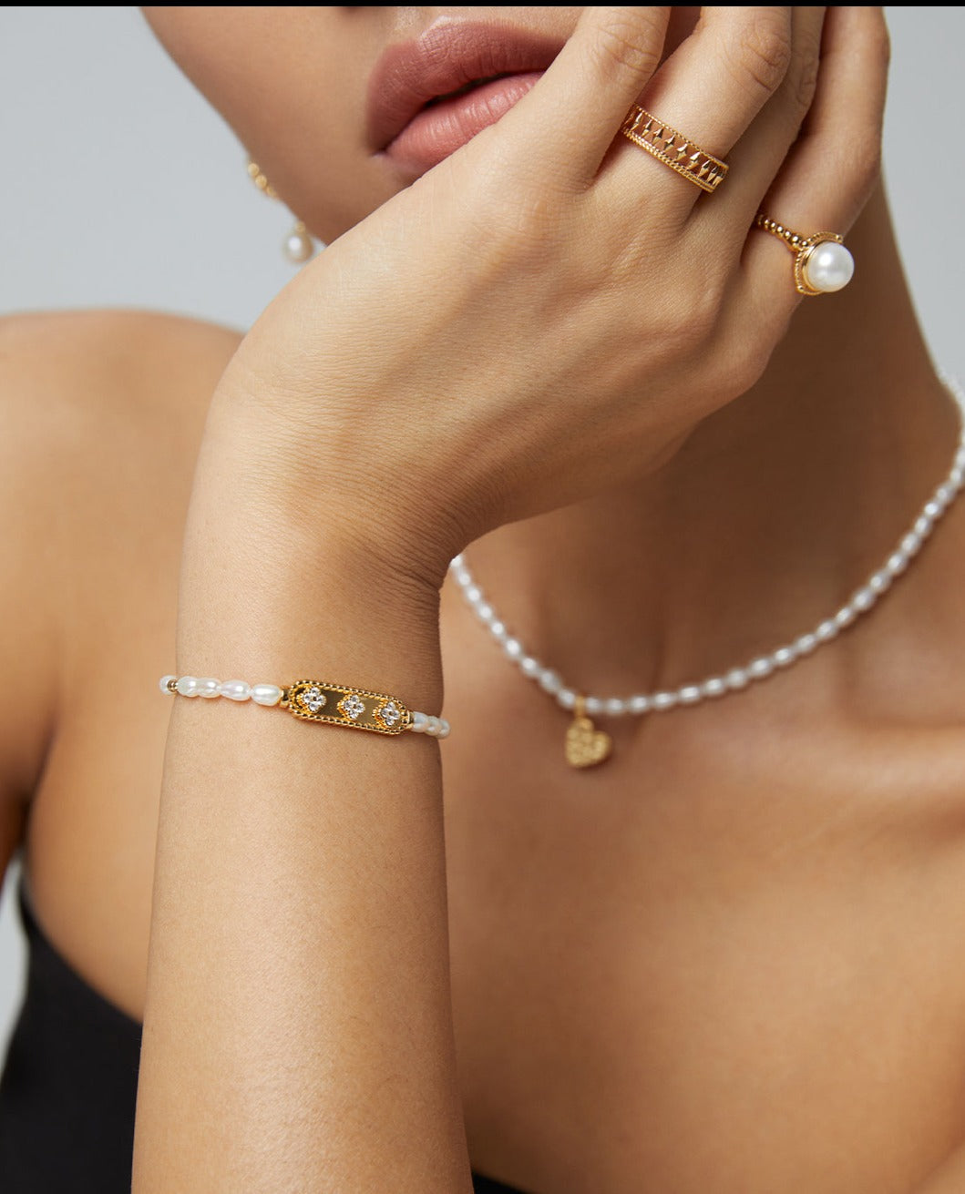 A stylish woman enhances her look with a gold bracelet and a pearl necklace.