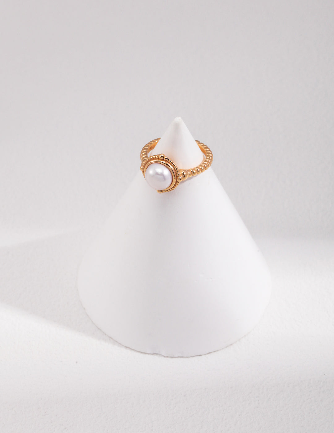 A stunning gold twisted band ring with a lustrous freshwater pearl on top, creating an elegant white centerpiece.