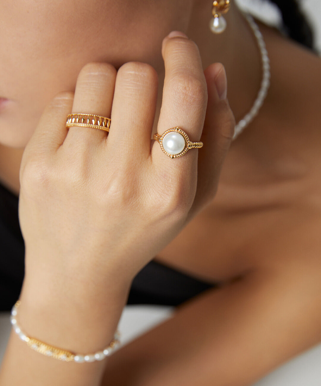 A woman wearing a gold twisted band freshwater pearl ring and a pearl necklace.