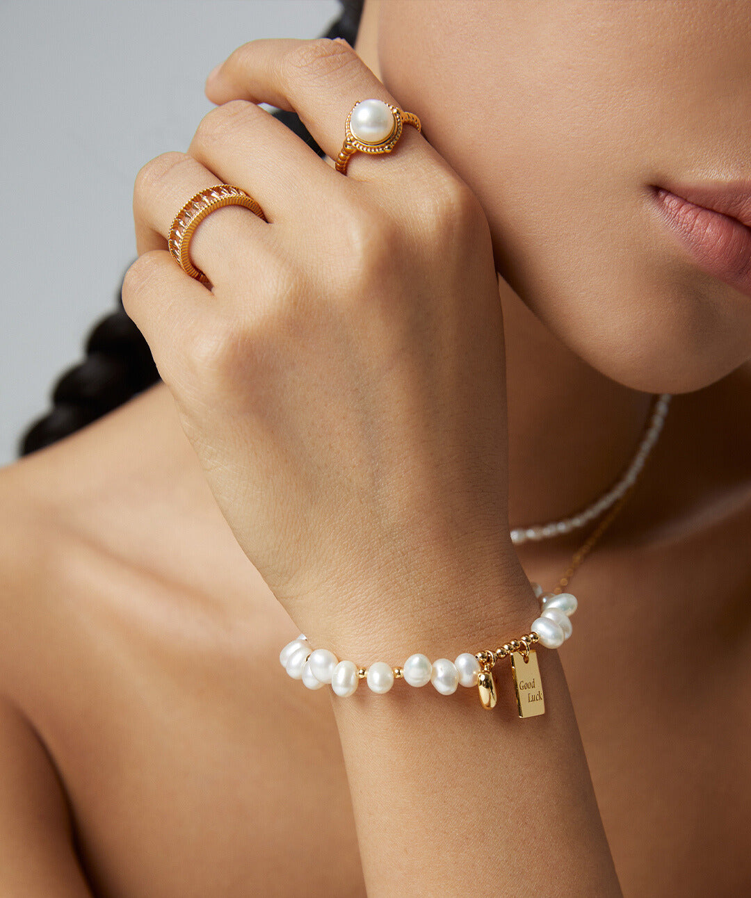 A woman wearing a gold bracelet and pearl bracelet, complemented by a gold twisted band freshwater pearl ring.