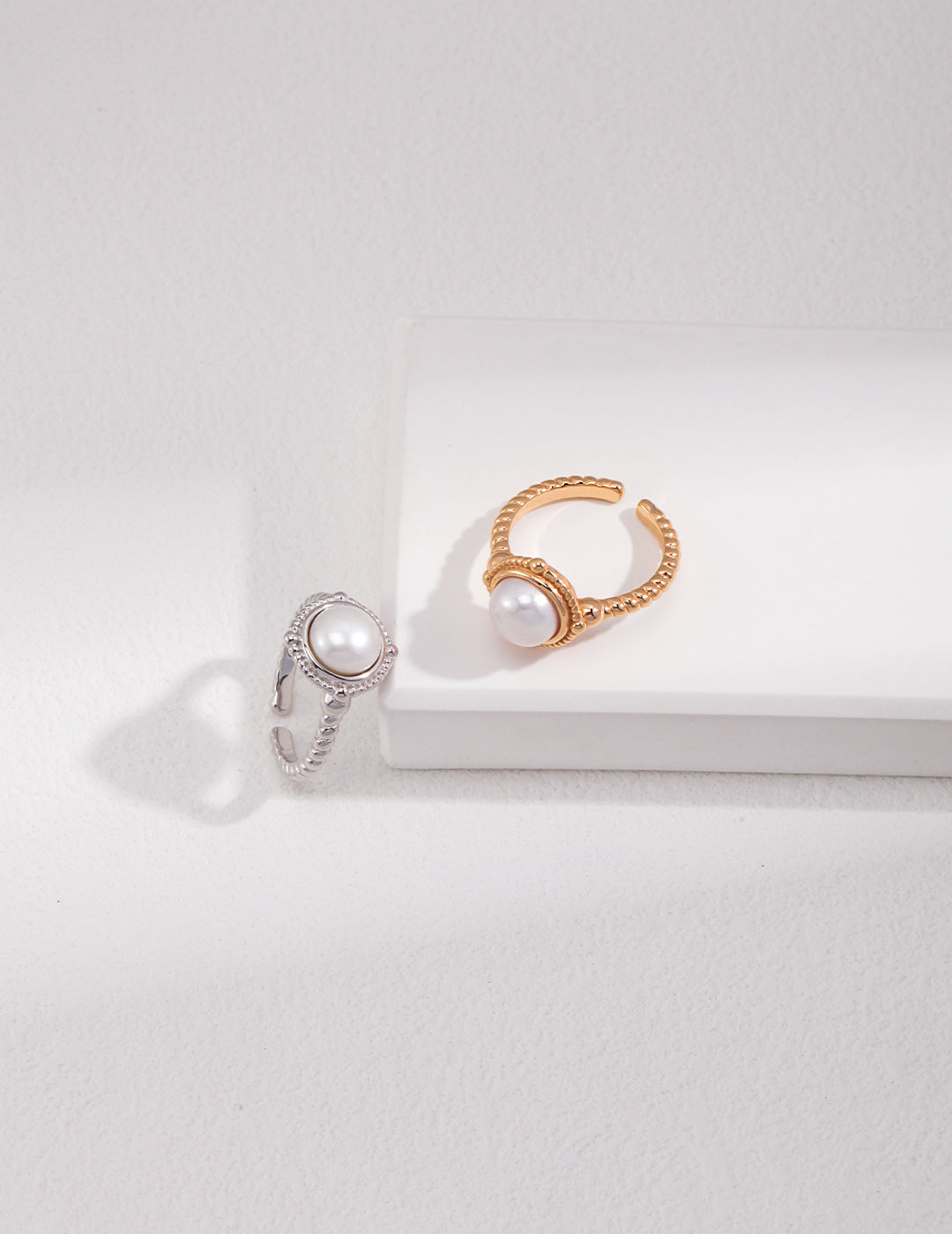 Two silver and gold twisted band freshwater pearl rings elegantly displayed on a pristine white surface.