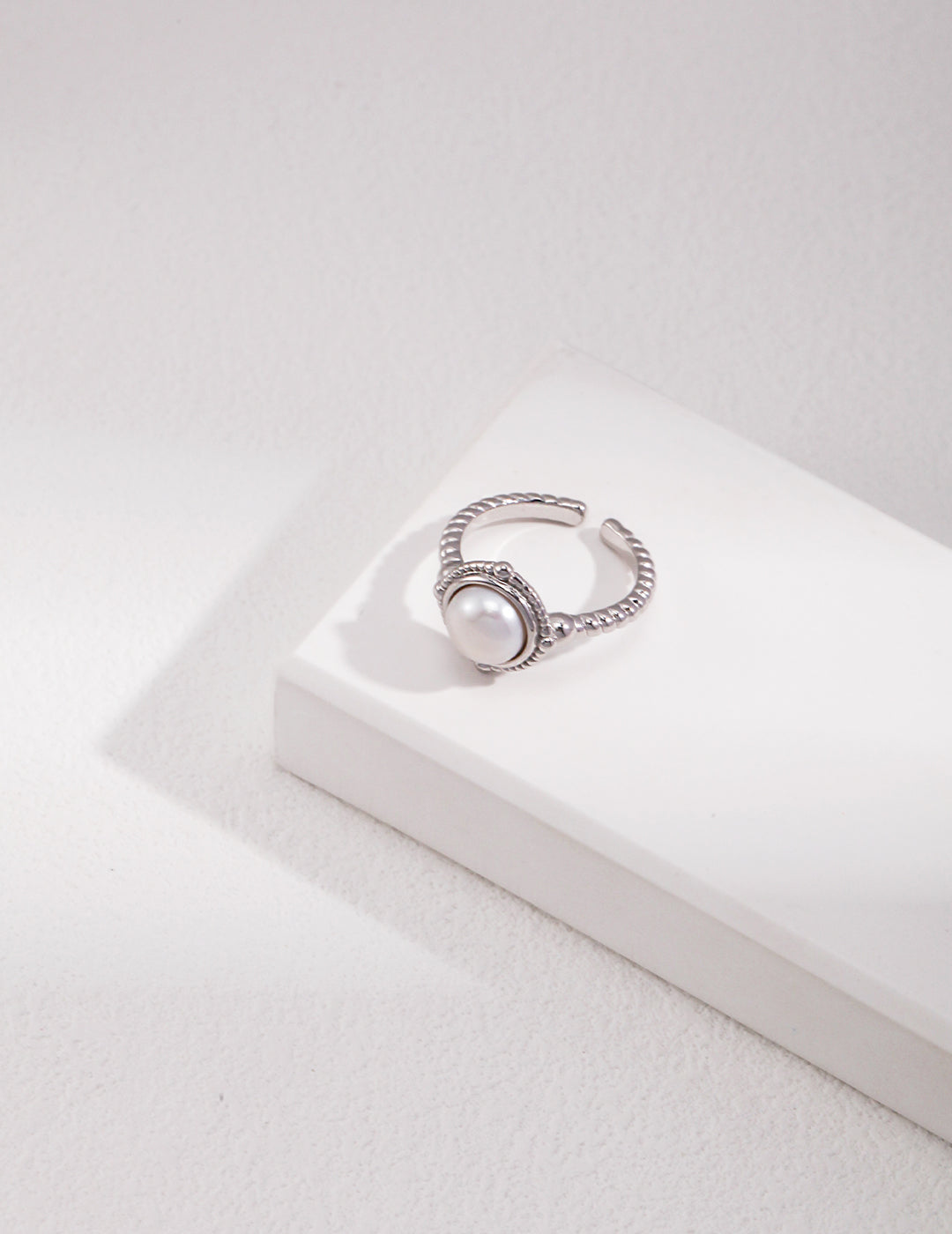 A silver twisted band freshwater pearl ring placed on a white box.