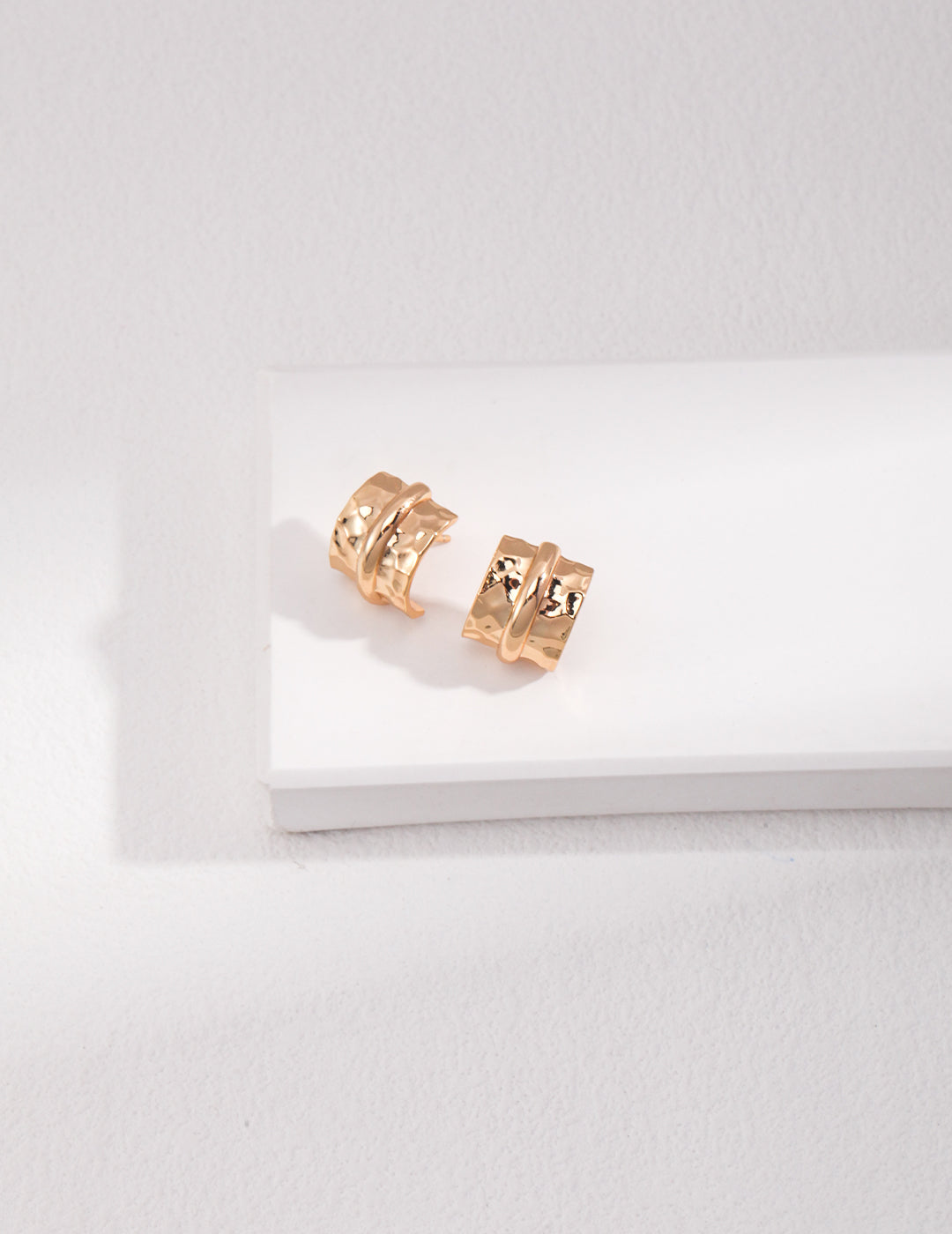 Mini gold chunky cuff earrings resting on white surface.